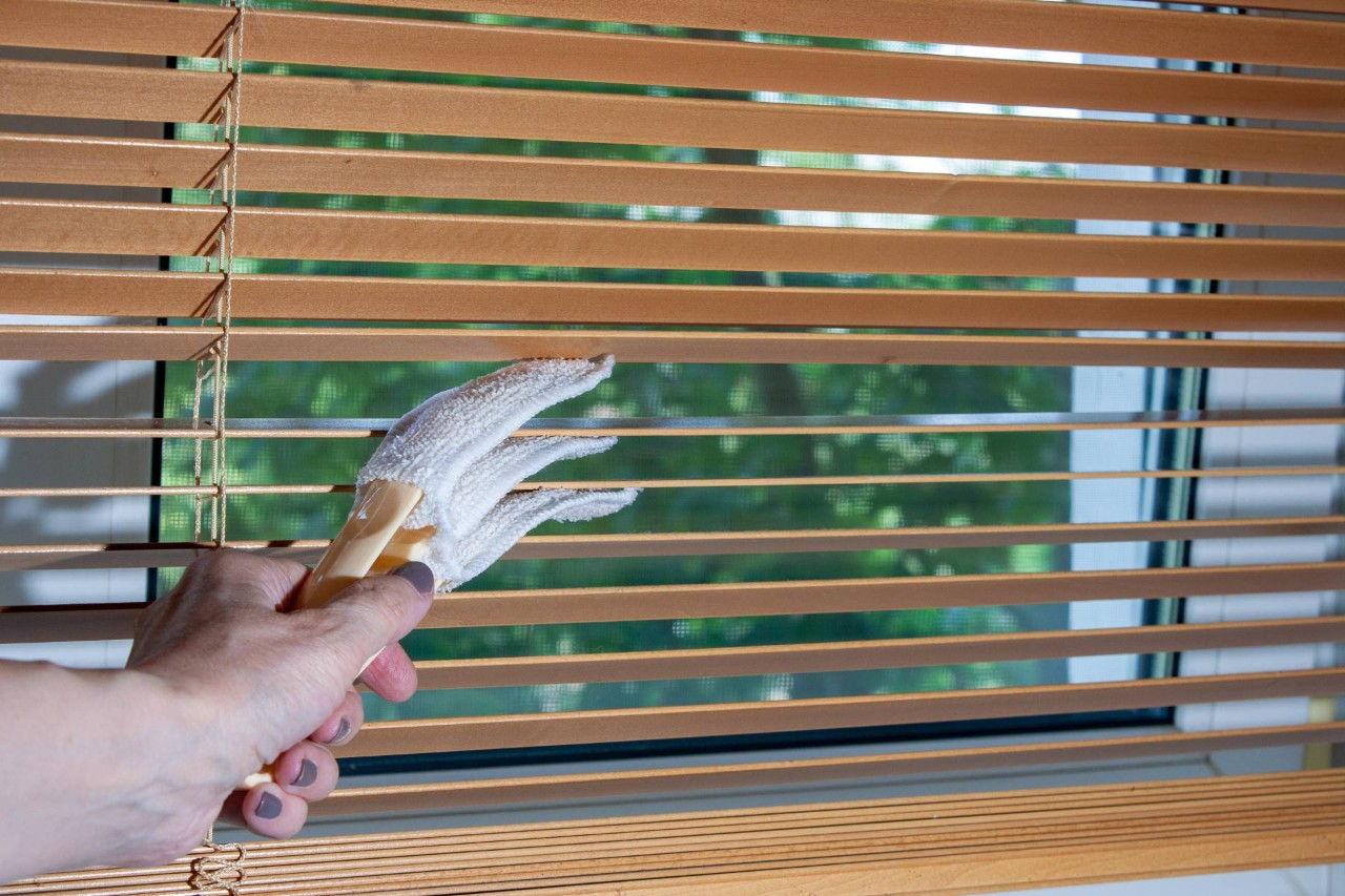 Person using a cloth duster to clean wooden blinds in their home